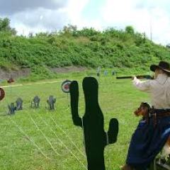 Person in cowboy attire shooting at targets in an outdoor range with cactus cutout.