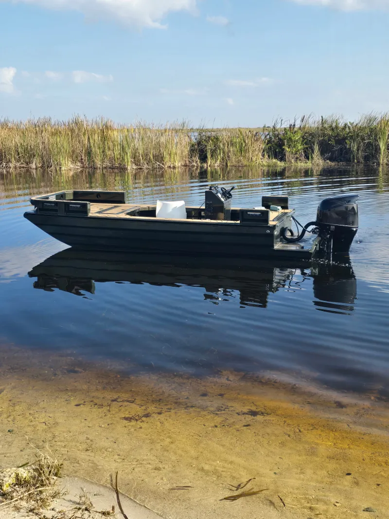 Small motorboat in calm water near a grassy shoreline under a clear blue sky.