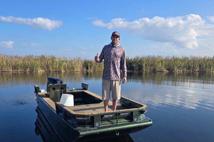 Person on a small boat in a calm body of water, with a blue sky and clouds in the background.