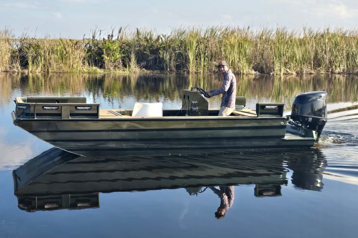 Man steering motorboat on calm lake under blue sky with clouds.