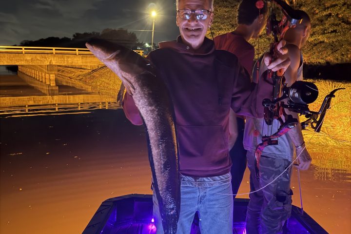 Man on boat at night holding large fish with purple lights.