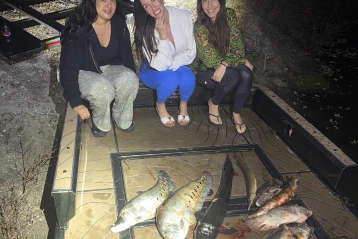 Three women smiling on a boat at night with various fish laid out in front of them.
